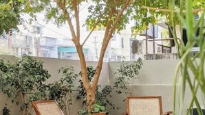 A patio with two wicker chairs, a potted plant, and a tree. - Mukam (Jaipur)