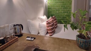 A kitchen with a green brick wall, white cushions, a coffee maker, a potted plant, and a mobile phone on the counter. - Mukam (Jaipur)