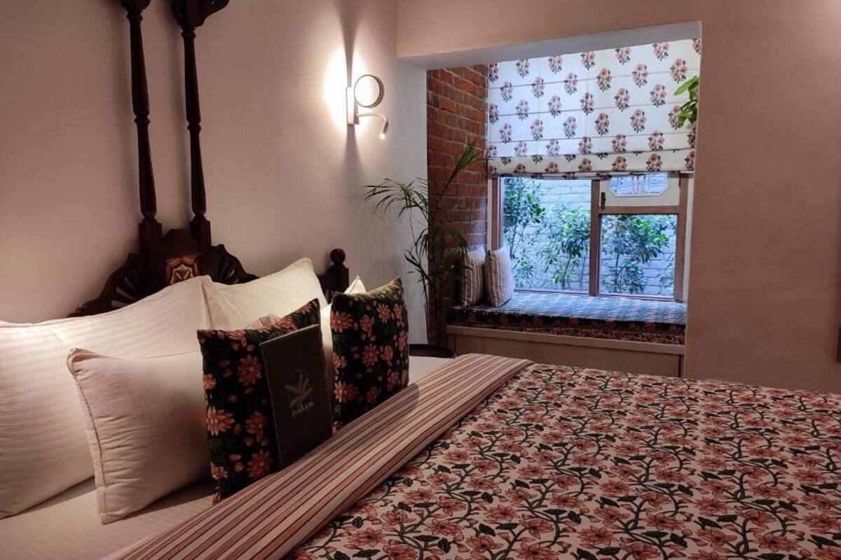 A bedroom with a bed, pillows, a bedside table, a nightstand, a window with a view, and a wall-mounted light fixture.