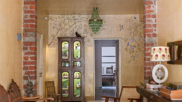 A room with a wooden cabinet, a chair, a table, and a hanging chandelier. - Mukam (Jaipur)