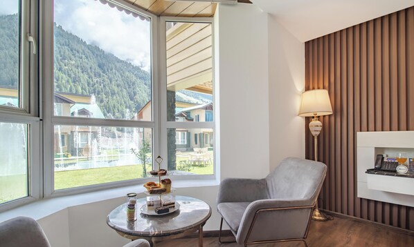 Una habitación con vista a una montaña y un lago, una mesa redonda con una lámpara y una silla.