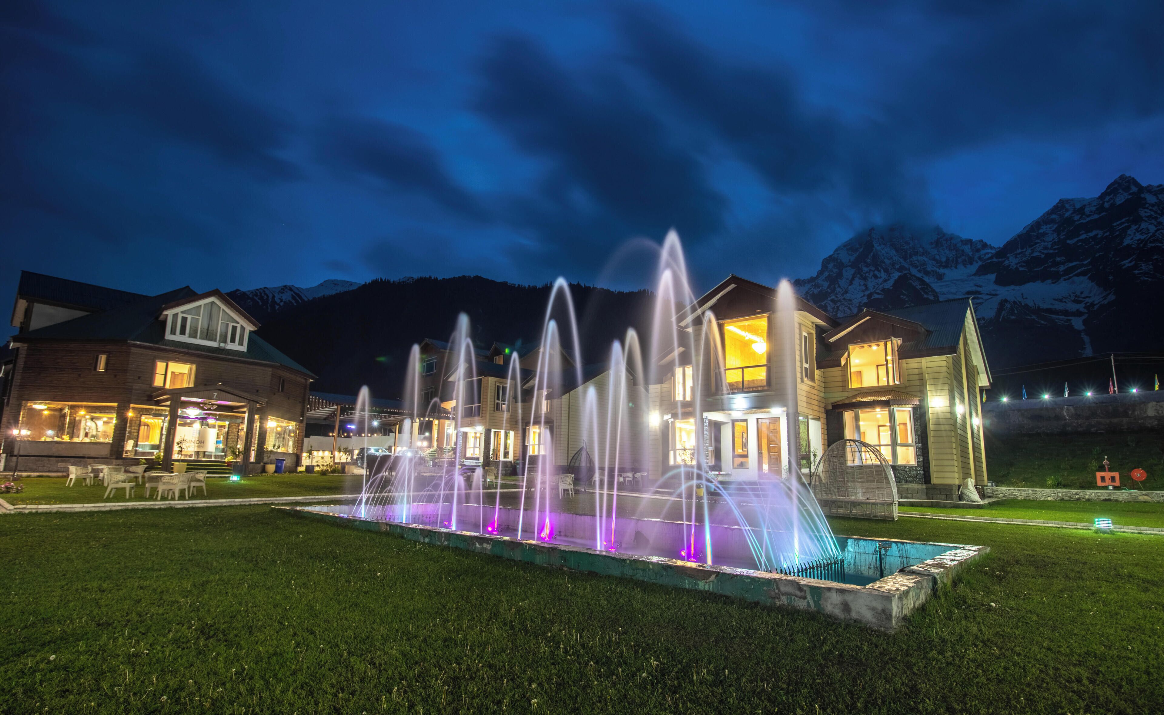 A hotel with a fountain, outdoor seating, and mountain views.