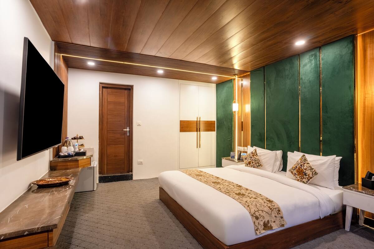 A hotel room with a large bed, a TV, a small kitchenette, and a wooden ceiling.