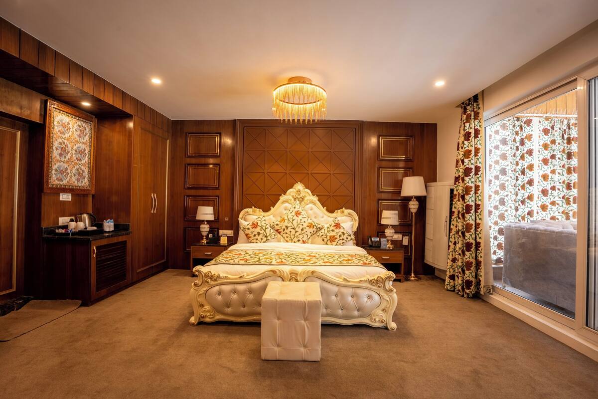 A bedroom with a large bed, a bedside table, a nightstand, a chandelier, and a window with curtains.
