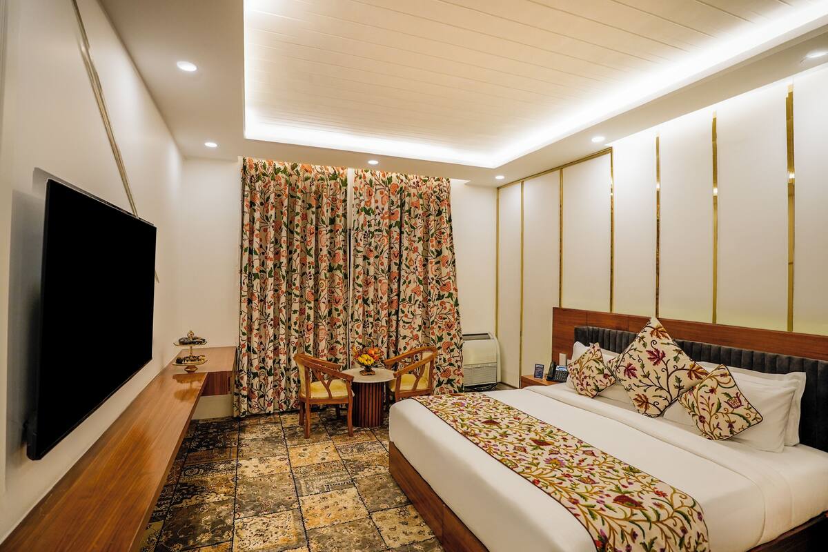 A hotel room with a bed, a TV, a desk with a chair, and a window with curtains.
