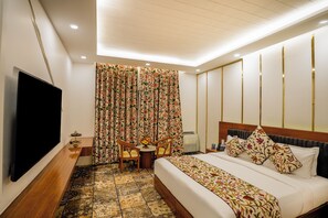 A hotel room with a bed, a TV, a desk with a chair, and a window with curtains. - Sindh Resort and Spa (Sonamarg)