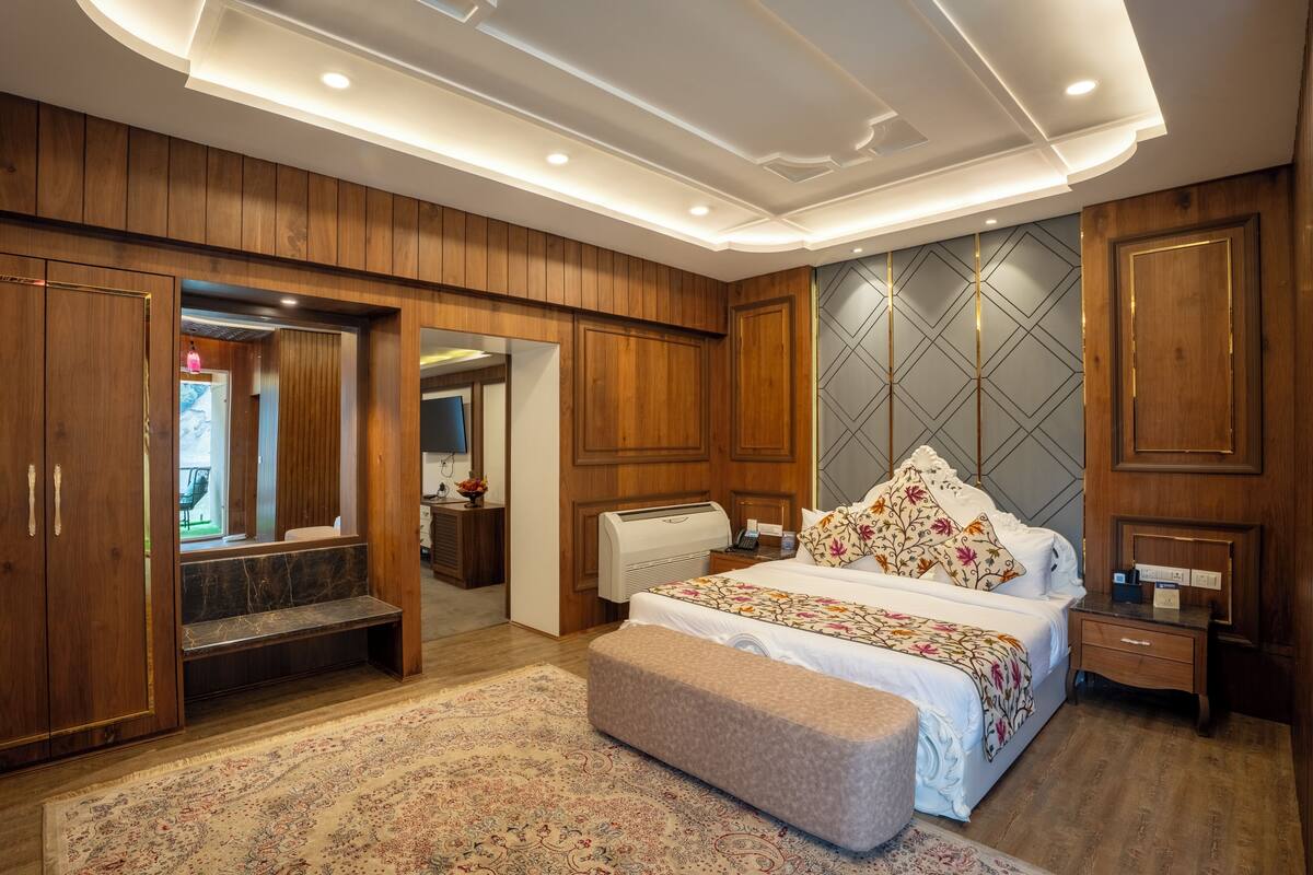 A bedroom with a large bed, wooden wardrobe, a bench, a bedside table, and a mirror.