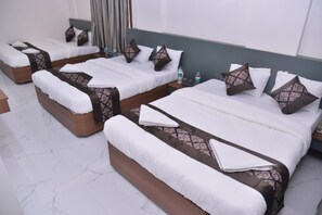 Una habitación de hotel con varias camas, cada una con cabecero, almohadas y una botella de agua sobre la mesita de noche.