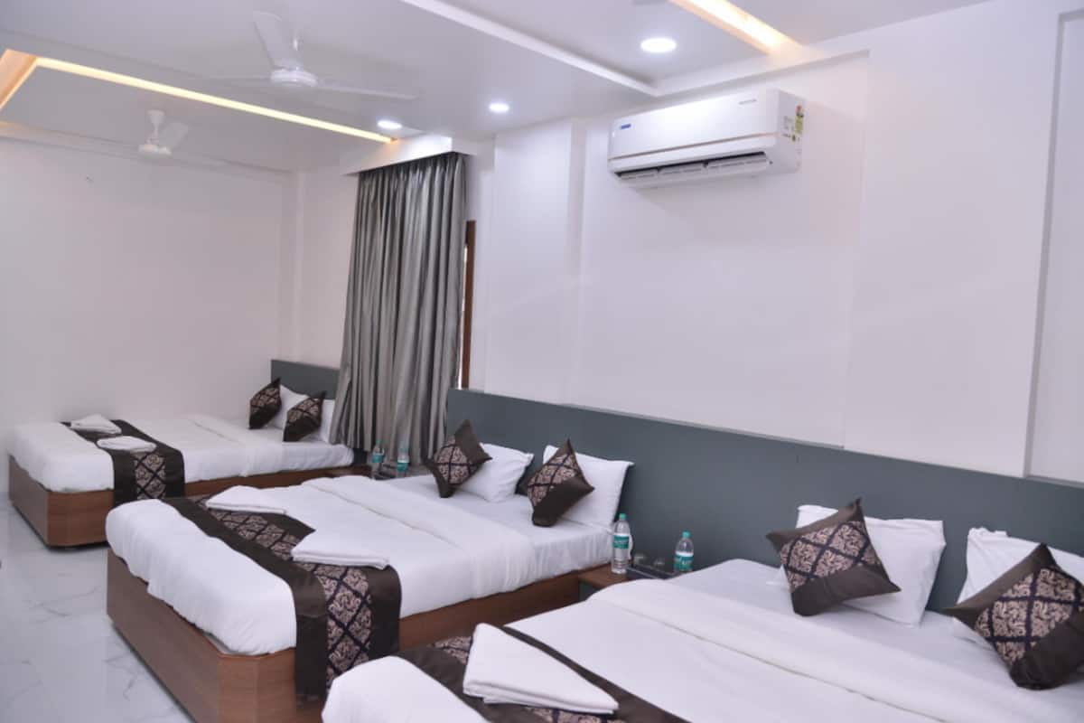 A hotel room with four beds, each with white linens and patterned pillows, a ceiling fan, an air conditioning unit, and a large window with curtains.