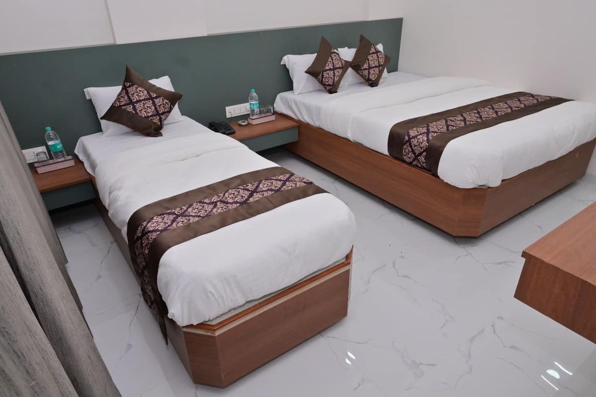Two twin beds with wooden frames and white bedding, a green headboard, a bedside table with a bottle and glasses, and a wooden nightstand.
