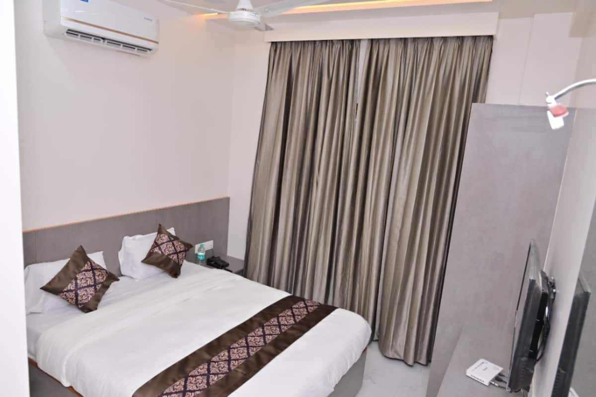A hotel room with a bed, curtains, an air conditioning unit, a ceiling fan, a TV, and a bedside table.