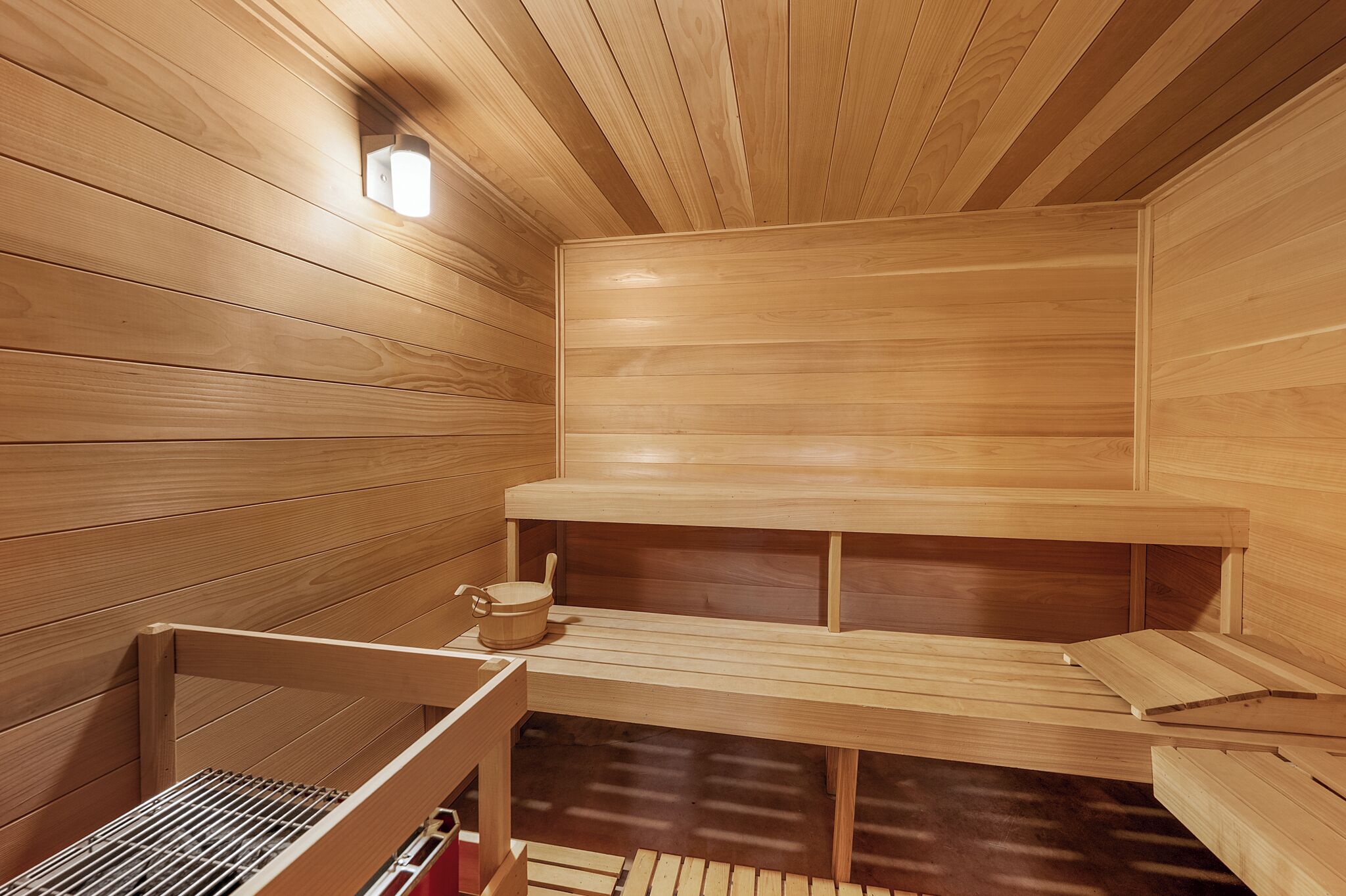 Una sauna con pareti e panche in legno, un lampadario e un piccolo contenitore di legno.