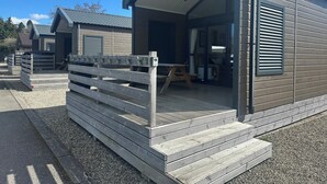 A small, single-story cabin with a covered porch, a wooden fence, and a gravel driveway. - Self-catering Lodge Inverness - Sleeps 4 (Inverness)