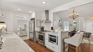 A modern kitchen with white cabinetry, stainless steel appliances, and a wooden dining area. - Hobnob - Private Pool - Golf Cart (Santa Rosa Beach)