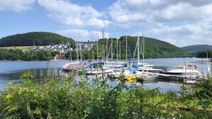 A calm lake with boats docked, surrounded by greenery and a bridge in the background. - diemelseeholiday Romantic Apartment with Balcony in the Sauerland near Willingen & Winterberg (Diemelsee)