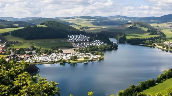 Blick auf einen See mit einem Campingplatz, Wohnmobilen, einer kleinen Insel und umliegenden HĂŒgeln.