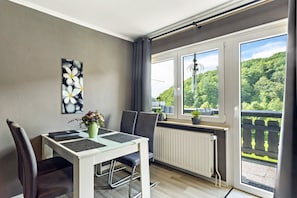 Ein Essbereich mit Tisch, Stühlen, einem Heizkörper und einem Fenster mit Blick ins Grüne.