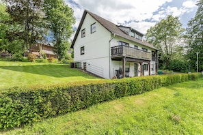 Ein zweistöckiges Haus mit Balkon, umgeben von gepflegtem Rasen und Hecken.