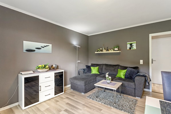 Ein modernes Wohnzimmer mit einer grauen Couch, einem weißen Schrank, einer Stehlampe und einem kleinen Tisch mit Dekoration.
