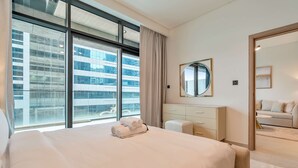 Hotellihuone, jossa on suuri sänky, lipasto, peili ja suuret ikkunat, joista on näkymä rakennukseen.
