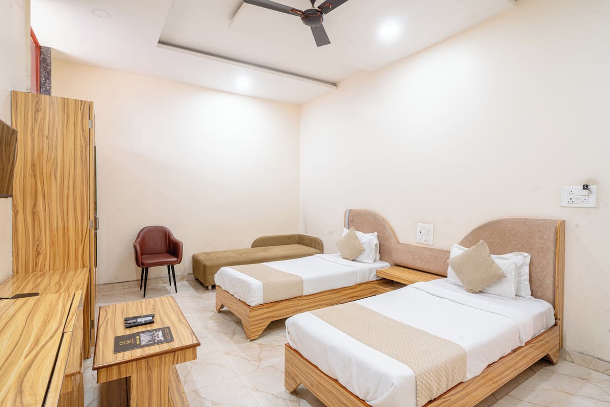 Une chambre d’hôtel avec deux lits en bois, une chaise rouge, une table en bois et un ventilateur de plafond.