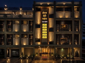 Un hotel de varios pisos con un letrero vertical central que enumera servicios como aire acondicionado, estacionamiento y un spa.