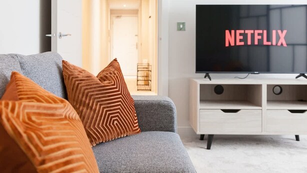 A modern living room with a grey sofa, orange patterned cushions, a white TV stand, and a large flat-screen TV displaying the Netflix logo. - Central Leeds Apartment Near Station - Sleeps 6 (Leeds)