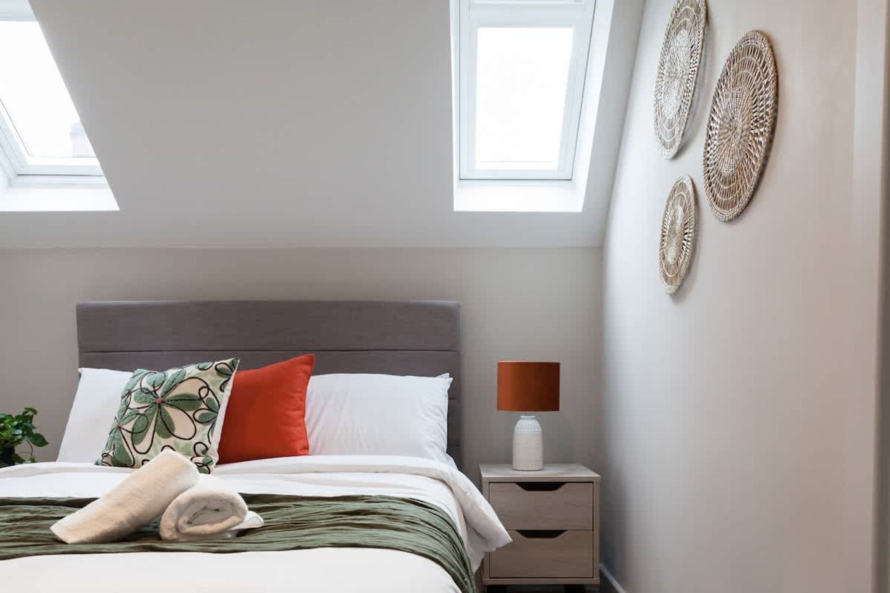 Une chambre à coucher avec un lit, des oreillers, une table de chevet, une lampe et des œuvres d’art murales.