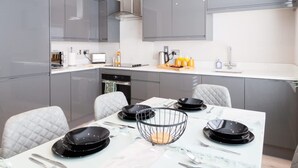 A modern kitchen with grey cabinets, a white countertop, and a dining table set with black plates and a wire basket. - Central Leeds Apartment Near Station - Sleeps 6 (Leeds)