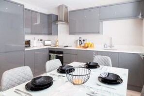 Una cocina moderna con armarios grises, una encimera blanca y una mesa de comedor con platos negros y una cesta de alambre.
