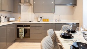 A modern kitchen with grey cabinets, a built-in oven, and a dining area with a table set for four. - Central Leeds Apartment Near Station - Sleeps 6 (Leeds)