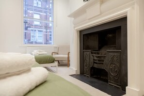 A room with a fireplace, a window, a bed with a green bedspread, and a chair. - Grand Central Leeds Apartment Near Train Station (Leeds)