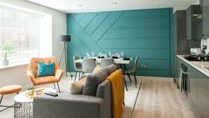 Eine moderne Küche mit einer Türkis-farbenen Akzentwand, einem Essbereich mit einem weißen Tisch und einer gemütlichen Sitzecke mit Sofa und Sesseln.