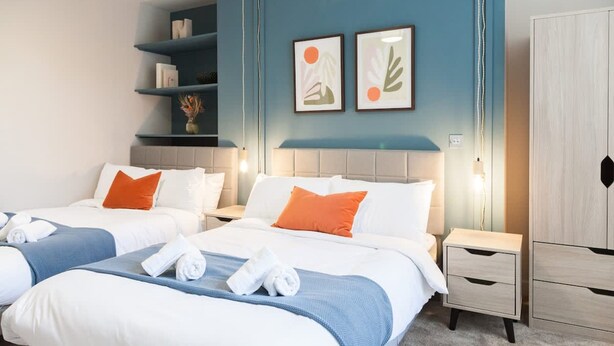 Ein Hotelzimmer mit zwei Betten, einem Nachttisch, einem Kleiderschrank und einer Wand mit Kunstwerken.