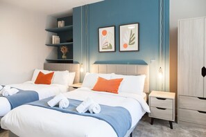 Ein Hotelzimmer mit zwei Betten, einem Nachttisch, einem Kleiderschrank und einer Wand mit Kunstwerken.