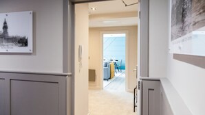 Ein Flur, der zu einem Zimmer mit Blick auf eine Stadtlandschaft führt, mit einem gerahmten Bild eines Gebäudes und einer Tür mit einem Metallgriff.