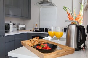 A modern kitchen with a breakfast tray, two glasses of orange juice, a kettle, and a bowl of strawberries. - Somers Suites Apartments-central-high Spec-sleep 4 (Leeds)