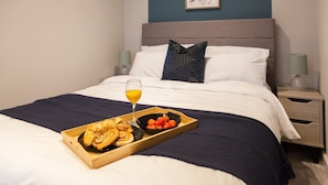 A neatly made bed with a tray of pastries and a glass of orange juice, a bedside lamp, and a framed artwork on the wall. - Somers Suites Apartments-central-high Spec-sleep 4 (Leeds)