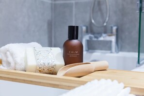 A bathroom with a shower, a bottle labeled 'CALM,' a bar of soap, a towel, and a wooden rolling pin on a wooden tray. - Somers Suites Apartments-central-high Spec-sleep 4 (Leeds)