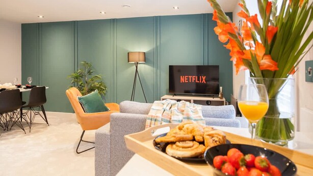 A modern living room with a sofa, a dining table, a TV displaying 'NETFLIX,' and a tray of food. - Somers Suites Apartments-central-high Spec-sleep 4 (Leeds)