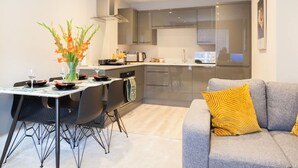 A modern kitchen with a dining area, a grey sofa with a yellow pillow, and a vase of flowers on the table. - Somers Suites Apartments-central-high Spec-sleep 4 (Leeds)