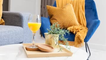 A living room with a blue armchair, a glass of orange juice, and a small plant on a table.