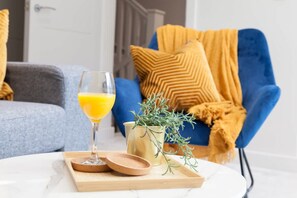 A living room with a blue armchair, a glass of orange juice, and a small plant on a table. - Somers Suites Apartments-central-high Spec-sleep 4 (Leeds)