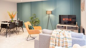 A modern living room with a dining area, a television, and a plant. - Somers Suites Apartments-central-high Spec-sleep 4 (Leeds)