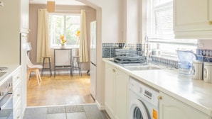 Een keuken met een wasmachine, een spoelbak en een raam met gordijnen.