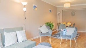 Een woonkamer met een bank, twee fauteuils, een salontafel en een eethoek met stoelen en een plant.