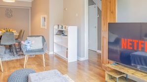 Een woonkamer met een televisie, een eethoek met stoelen en een tafel, en een trap die leidt naar een andere kamer.