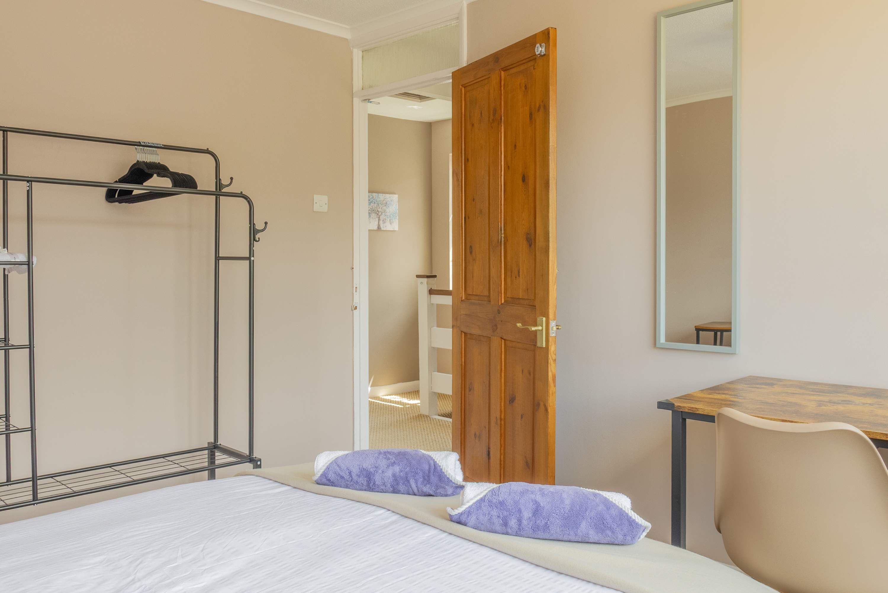 A room with a bed, a wooden door, a mirror, and a small table.