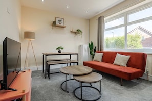 Ein Wohnzimmer mit Fernseher, Sofa, zwei kleinen Tischen, einer Lampe und einem Fenster mit Blick.