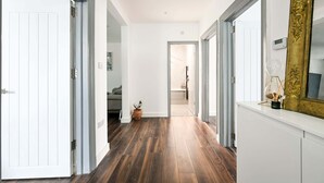 A hallway with wooden flooring, white walls, and a large mirror on the right. - 3 Bed House Near Epping Forest Greater London (London)